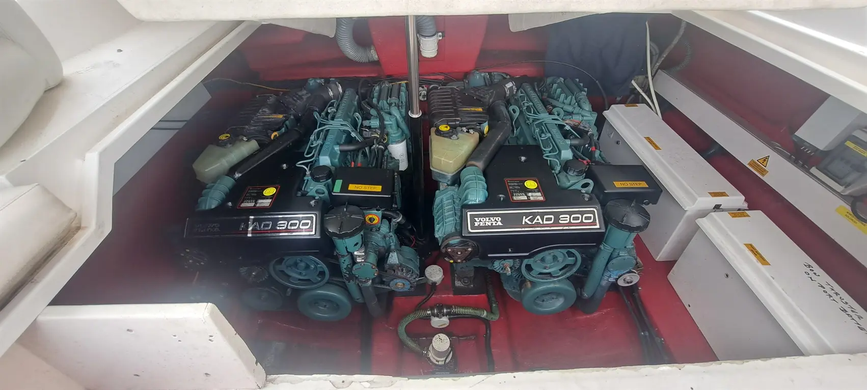 Two Volvo Penta KAD 300 engines in a boat's engine compartment, with visible warning labels and maintenance equipment nearby.